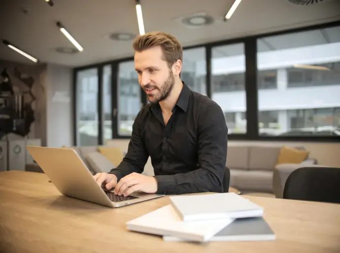 Professional smiling while reviewing data on a laptop and holding a coffee cup in a modern office / HSO Trading