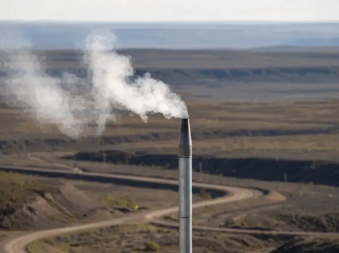 Industrial flare stack emitting white plume in an oil field landscape / HSO Trading