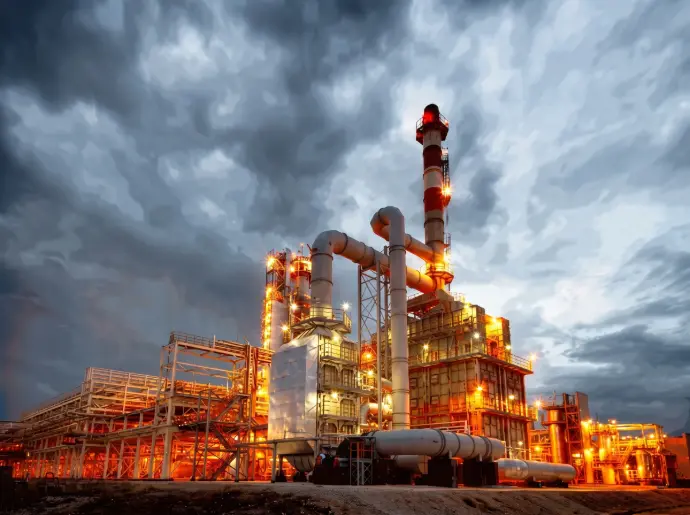 Industrial oil refinery facility at night with illuminated storage tanks / HSO Trading
